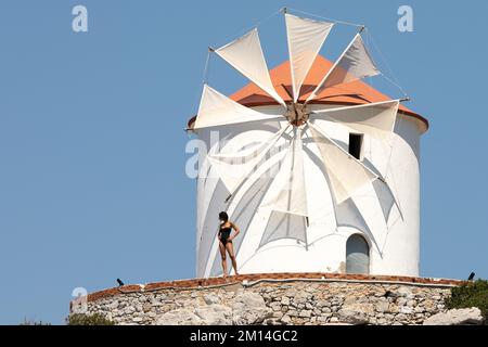 A woman in a black swimsuit standing in front of a windmill. Stock Photo