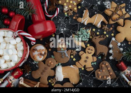 Homemade gingerbread Christmas cookies, gym workout dumbbell, hot chocolate or cocoa with marshmallows, candy canes. Fitness winter diet flat lay. Stock Photo