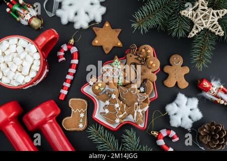 Homemade gingerbread cookies, gym workout dumbbells, hot chocolate cocoa with marshmallows, Christmas tree decorations. Fitness winter diet flat lay. Stock Photo