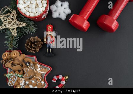 Gingerbread cookies, gym workout dumbbells, chocolate cocoa with marshmallows, Christmas decorations. Fitness winter diet, flat lay with copy space. Stock Photo