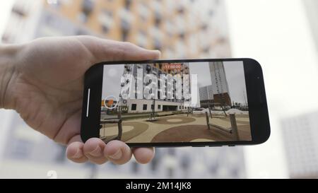 Detail view of a hand holding a smartphone device and making a video of a multi storey house and children playground. Close up of using smartphone for Stock Photo