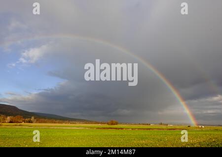 amazing rainbow on dark rain clouds over green fields in the winter Stock Photo