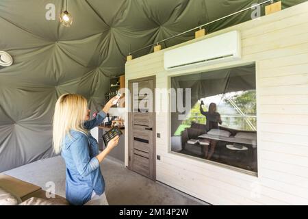Young woman using smartphone home application on tablet computer when setting temperature in her apartment Stock Photo