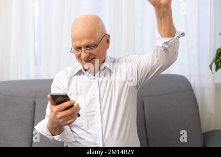 Excited elderly mature retired man looking at telephone screen, celebrating online lottery win or getting message with good news. Emotional mature Stock Photo