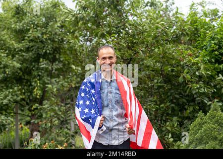 Attractive man holding Flag of the United States on blue sky background on a clear, sunny day. View from the back, close-up. National holiday concept Stock Photo