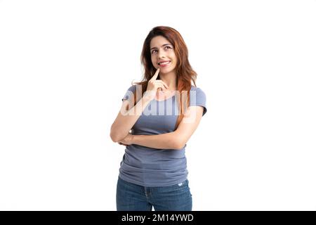 A studio shot of a thinking happy female with an arm on her chin on a white background Stock Photo