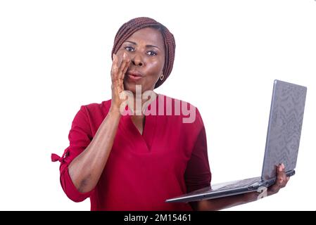 a beautiful businesswoman in a red camisole standing on a white background holding laptop hand with whispering mouth. Stock Photo