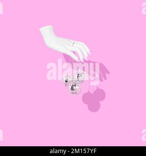 A woman's hand holding disco balls on pink background Stock Photo