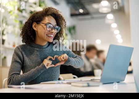 Smiling african woman speaks sign language with friends by video call while sitting in cozy cafe Stock Photo