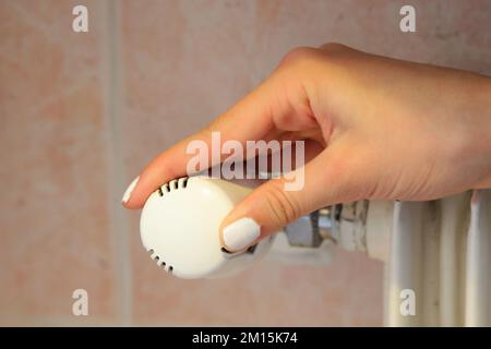 Hand regulating the white Thermostatic Valve for setting the temperature of the radiators for energy saving Stock Photo