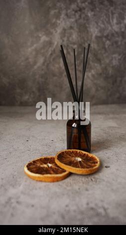Citrus reed diffuser on dark background. Creating cozy atmosphere at home. Bottle, sticks and dry oranges. Vertical photo Stock Photo
