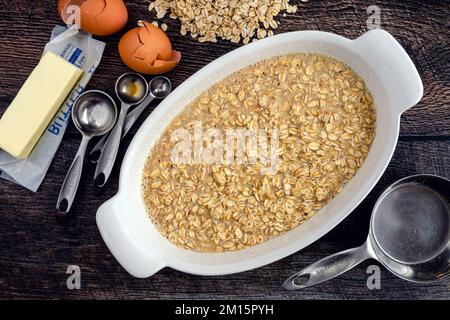 Rolled Oats, Milk, and Other Baked Oatmeal Ingredients in an Oval Baking Dish: Uncooked oatmeal viewed from overhead and surrounded by ingredients Stock Photo