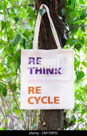 Environmentally friendly bag with Rethink Recycle written on surface hanging on tree trunk in green forest in summer Stock Photo
