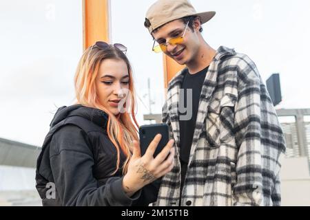 Low angle of young man and woman in stylish clothes watching video on cellphone while spending time on city street together Stock Photo