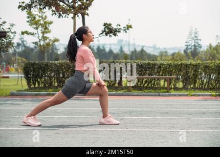 Side view full body of young female athlete in activewear with ponytail doing lunge exercise during fitness training on stadium Stock Photo