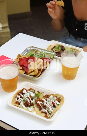 From above of appetizing nachos with salad and tacos with sauce on plates served with glasses of beer in restaurant Stock Photo
