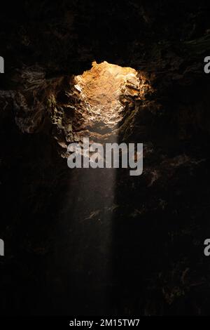 From below view of lonely sunray shining through descent into stony cave located in Lanzarote Stock Photo