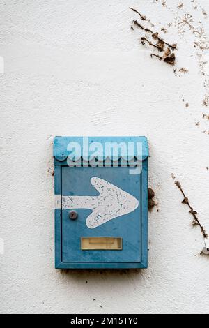 Exterior plaster white wall of house with hanging blue shabby mail box with white arrow Stock Photo