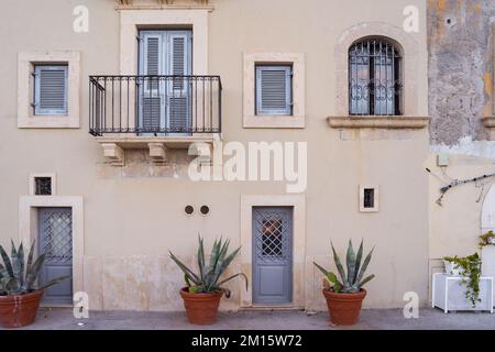Facade of old residential building with windows and green potted plants placed near wall under balcony in Syracuse Stock Photo
