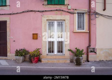 Facade of old residential building with windows and green potted plants placed near pink wall under balcony in Syracuse Stock Photo