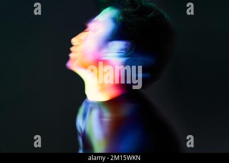 Side view of long exposure artistic creative portrait of man in multicolored neon lights on black background Stock Photo