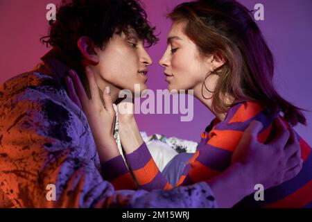 Side view of crop young amorous man and woman in casual clothes standing looking at each other in projector light Stock Photo