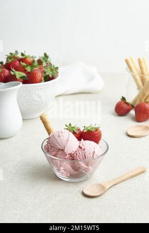 Delicious homemade strawberry ice cream scoops served in glass bowl with berries and waffle roll in kitchen in daylight Stock Photo