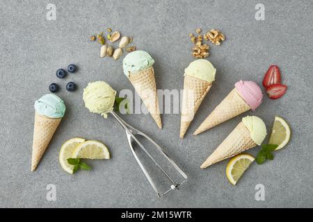 Top view of assorted appetizing ice cream cones with blueberry pistachio walnuts strawberry and lemon composed on gray table with ingredients in kitch Stock Photo