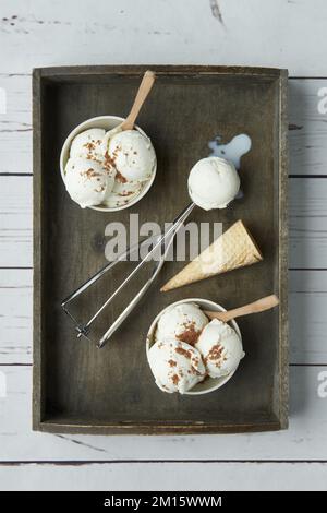 Top view of scoops of delicious ice cream with cinnamon powder served in bowls and placed on wooden tray near waffle cone in kitchen Stock Photo