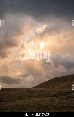 Scenic view of sun shining through clouds on mountain ridge covered with grass Stock Photo