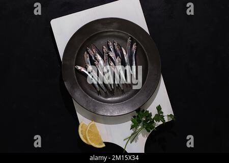 Top view of raw small fishes in plate on white board on black background Stock Photo