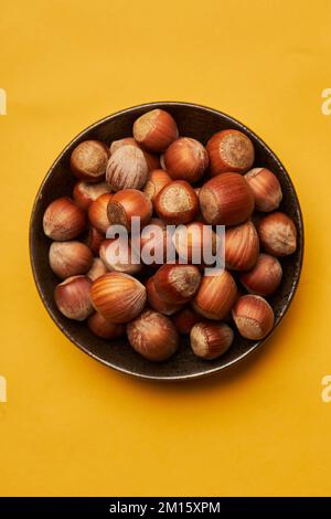 Top view of fresh unpeeled hazelnuts placed in bowl on yellow background Stock Photo