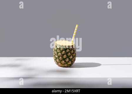 Ripe pineapple with striped straw placed on sunlit table symbolizing fresh healthy drink on gray background Stock Photo