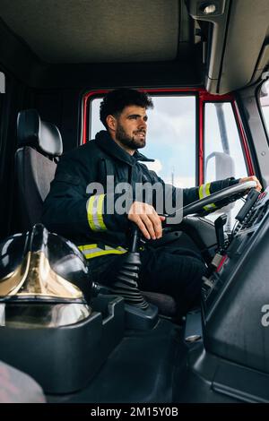 Fireman with helmet sitting on driver seat of fire engine during work in daytime Stock Photo