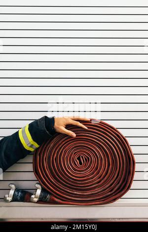 Anonymous fireman in protective workwear touching rolled up hose placed on side of fire engine Stock Photo