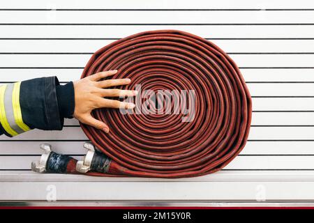 Anonymous fireman in protective workwear touching rolled up hose placed on side of fire engine Stock Photo