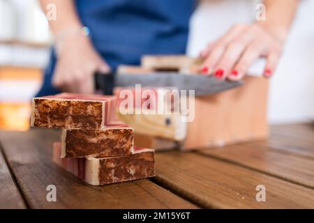 Crop anonymous female seller cutting pieces of eco friendly soap on wooden table in workshop Stock Photo