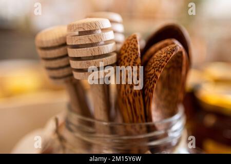Closeup of wooden honey scoops and spoons placed in glass jar on blurred background Stock Photo