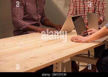 Three anonymous people Working on a Wooden Table with laptops Stock Photo