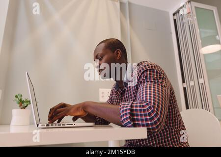 Black Man working with a laptop on a Wooden Table Stock Photo