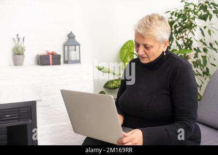 Front view concentrated pleasant mature older woman looking at computer screen. Happy middle aged lady web surfing information, ordering food online Stock Photo