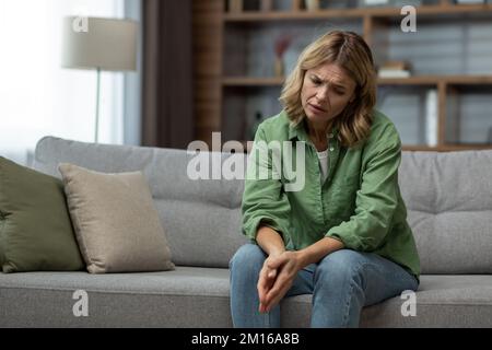 Sad senior mature woman sitting on sofa in living room wife grieving divorce depressed. Stock Photo