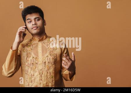Young brunette indian man talking on cellphone isolated over yellow background Stock Photo