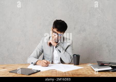 Young serious indian businessman working with paper documents while sitting at table in office Stock Photo