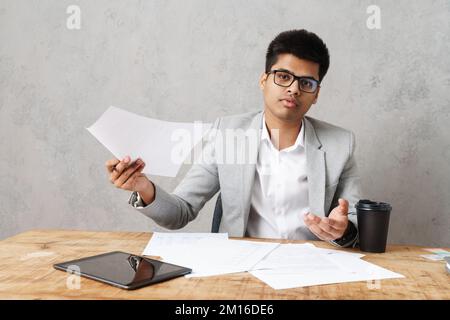Young serious indian businessman working with paper documents while sitting at table in office Stock Photo
