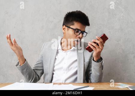 Young serious indian businessman using cellphone while working with paper documents in office Stock Photo
