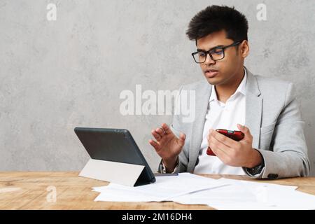 Young serious indian businessman using tablet computer and cellphone while working in office Stock Photo