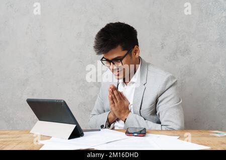 Young happy indian businessman using tablet computer while working with paper documents in office Stock Photo