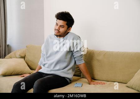 Young indian man relaxing and sitting on the sofa next to his phone in cozy room at home Stock Photo