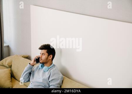 Young indian man sitting on sofa and talking on his phone Stock Photo
